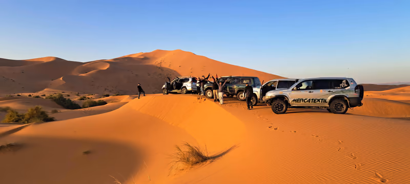 A 4x4 convoy paused on the dunes, arms raised at golden hour