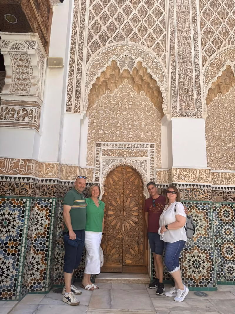 Travelers posing by the carved cedar door of a Marrakech medersa